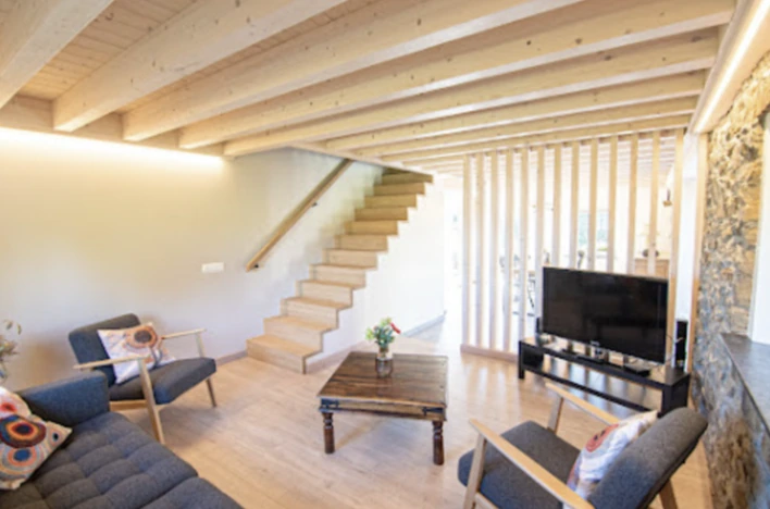 Vue du salon depuis le bas de l’escalier, avec les fauteuils, le canapé et le mur en pierre
